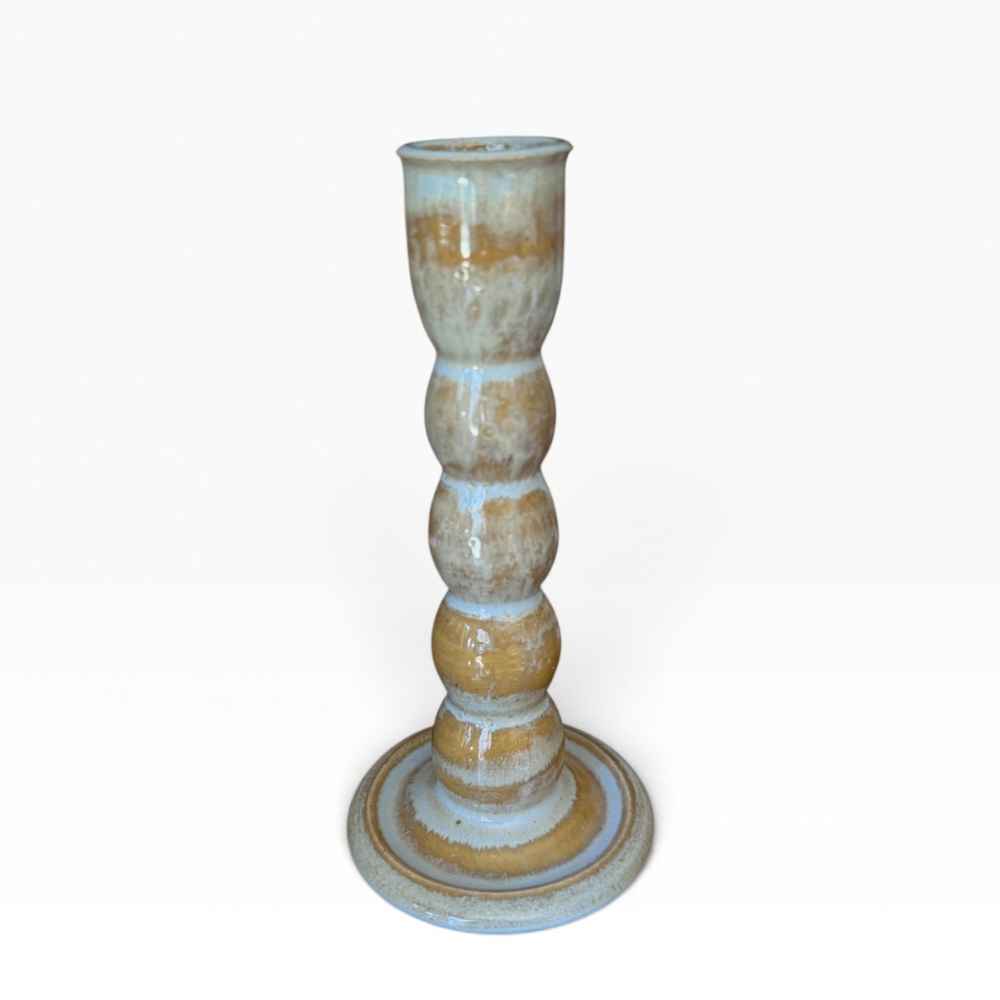 A tall, multi-tiered banded ceramic candlestick holder with a rustic glazed finish in light blue / green and warm tan tones, set against a plain white background.