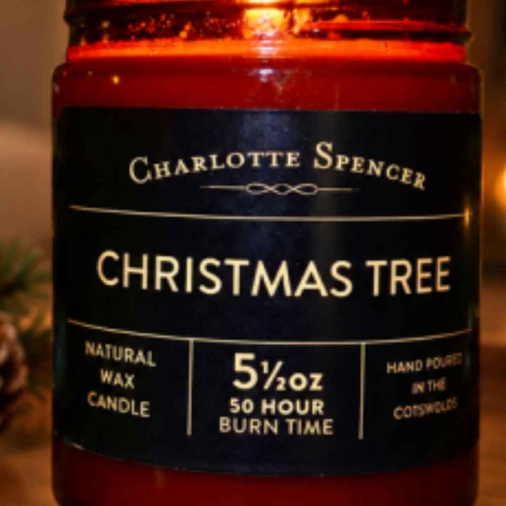 Charlotte Spencer Christmas Tree natural wax candle in a dark amber glass jar with a black label and gold lettering, shown close-up with warm orange candlelight.