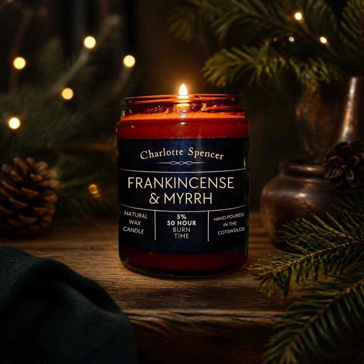Frankincense and myrrh candle in brown glass jar surrounded by Christmas lights and foliage